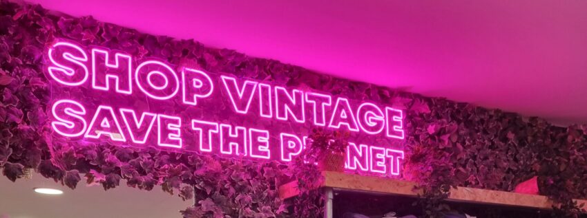 The picture shows a bright pink neon sign that says: Shop vintage save the planet.